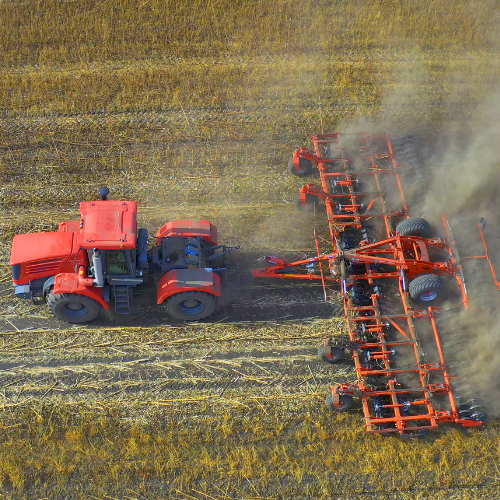 Picture of tractor dragging combine harvester over field.
